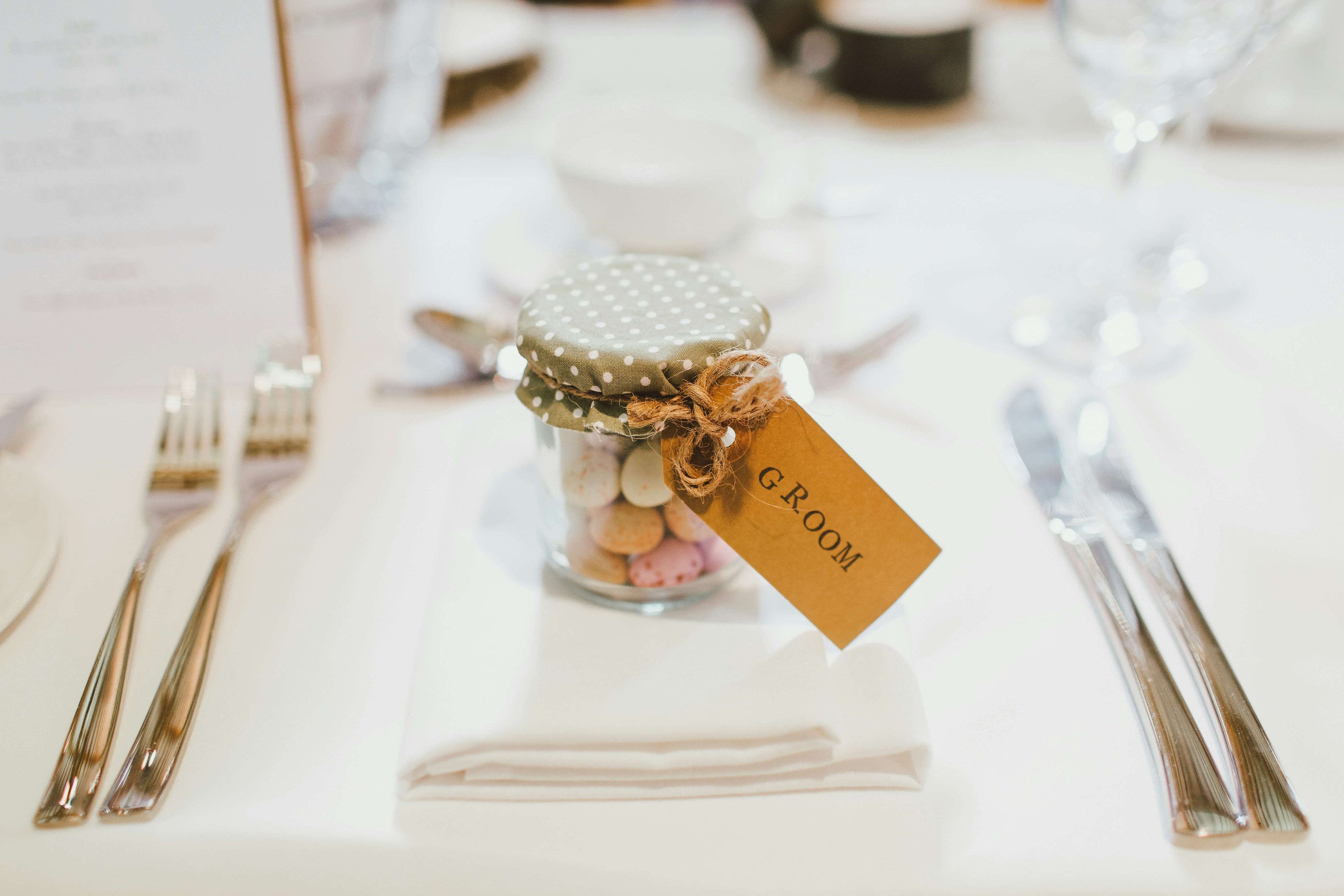 Small glass jar with candies and a 'Groom' tag on a table setting.
