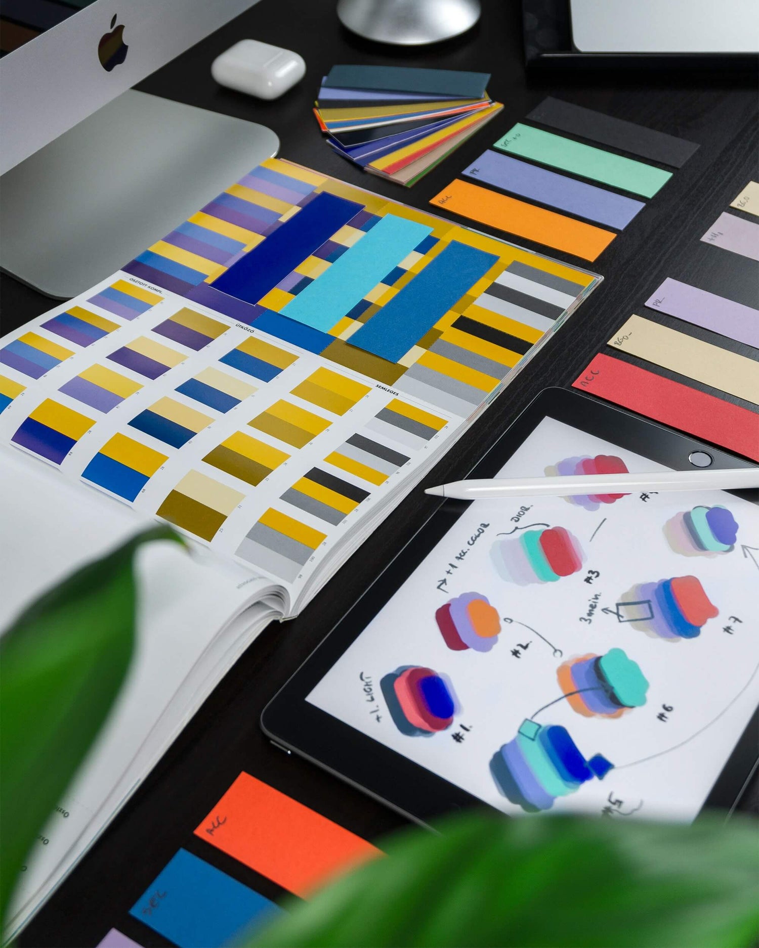 Color swatches and design tools on a desk with a tablet displaying colorful graphics.